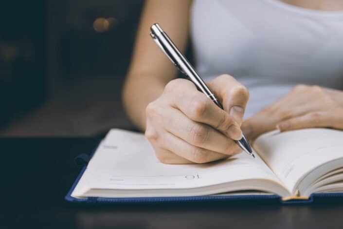 woman in white top writing on notebook