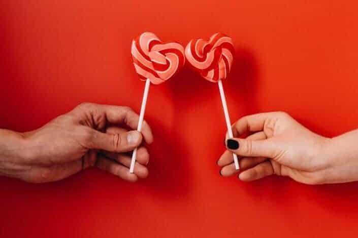 Two heart shaped pink and red stripped lollipop held by a man and a woman