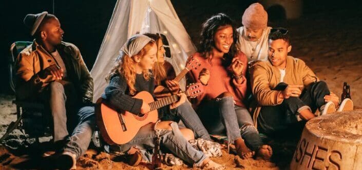 Group of friends on a camping singing with a guitar while gathered around their campfire