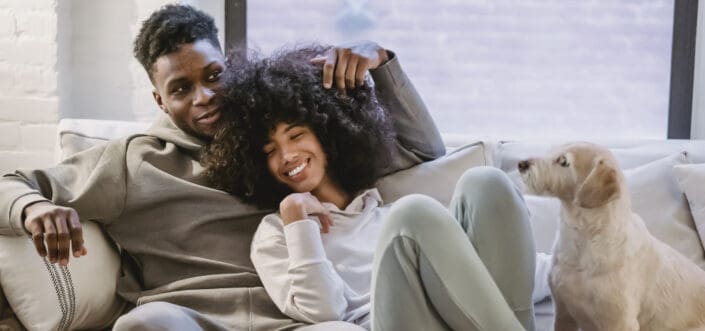 Couple cuddling on a couch with their pet.