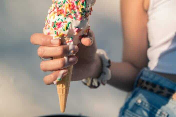 An ice cream topped with sprinkles melting in a hand 
