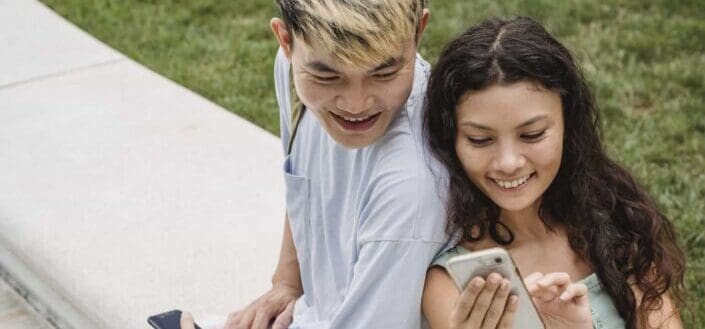 Charming ethnic woman showing smartphone to Asian partner.