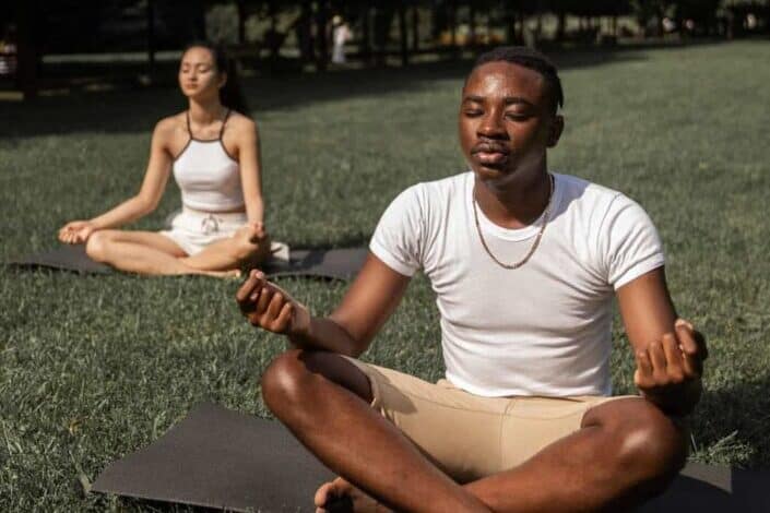 Multiethnic couple meditating together in park.