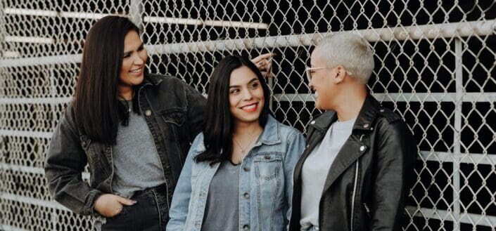 3 women standing beside gray metal fence