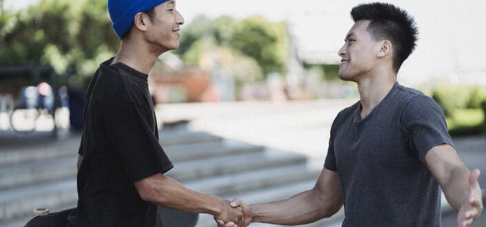 Two men shaking hands on sunny street.