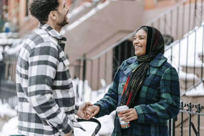 Ethnic laughing couple holding hands standing on street