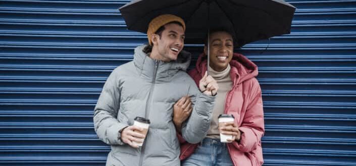 Joyful diverse couple with coffee on rainy day