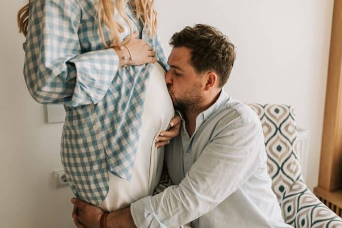husband hugging and kissing wife's pregnant belly