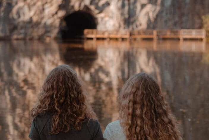 Women Sitting on Ground Facing Body of Water