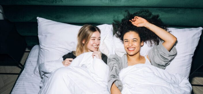 Women Having Fun While Lying on White Bed