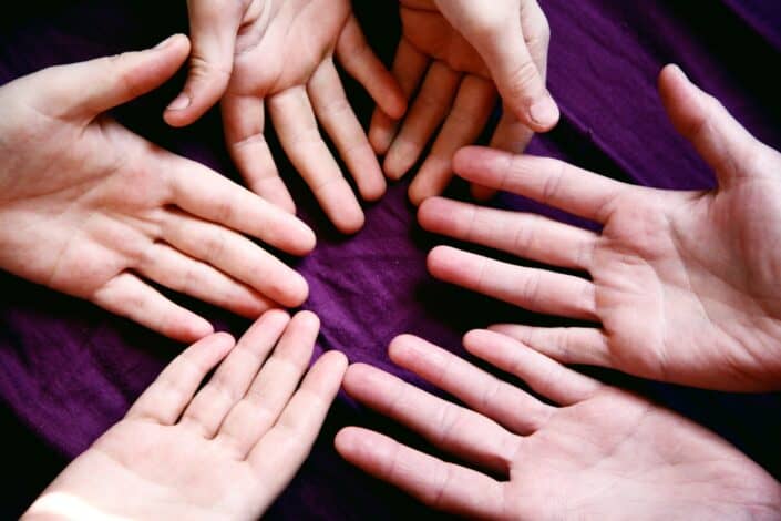 hands of three people laid on top of a purple cotton