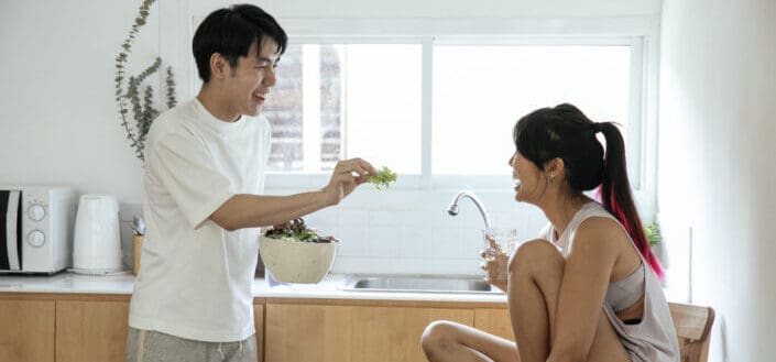 Couple having some fun while eating salad in their cozy kitchen