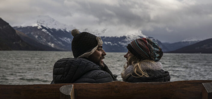 Couple sitting in a wooden bench enjoying the cold weather beside a lake
