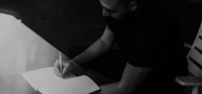 man in black writing on white paper