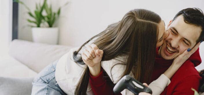 Guy playing video games distracted by a kissed from her girlfriend