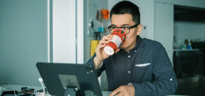 Man drinking coffee while working on his computer.