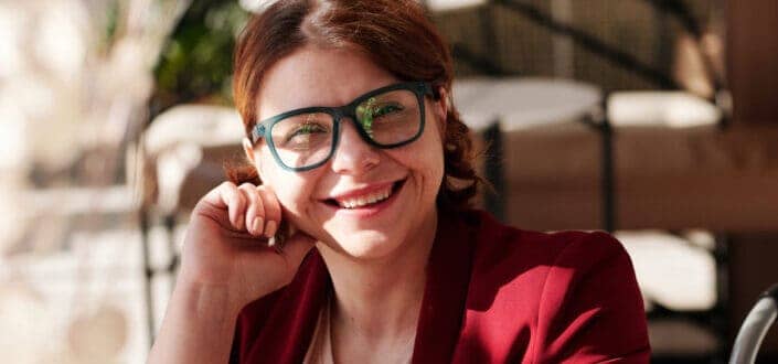 A smiling woman wearing big reading glass and red blazer