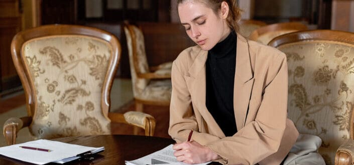 Woman in a beige formal jacket and black turtle neck signing on a document