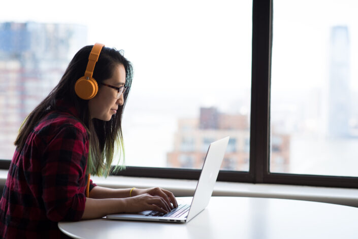 Woman wearing an orange headphone working with her laptop