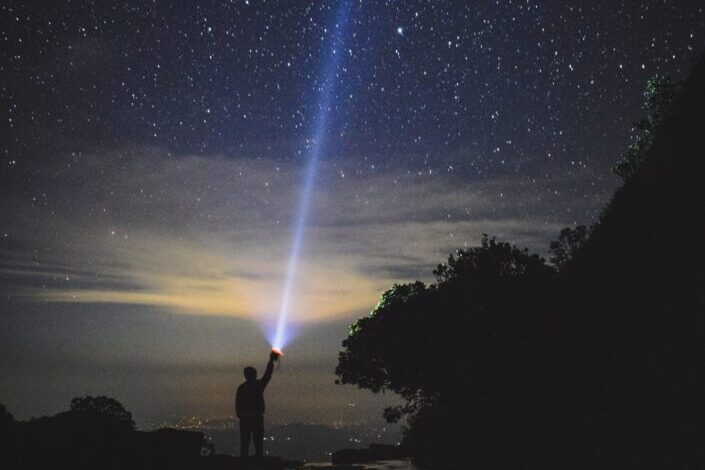 A person holding a flashlight pointing towards the sky.