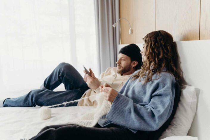Couple knitting together on the bed.