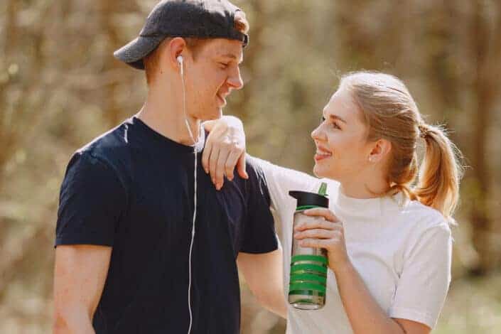 Guy earing a black cap and blue shirt staring at her girlfriend holding a sports bottle