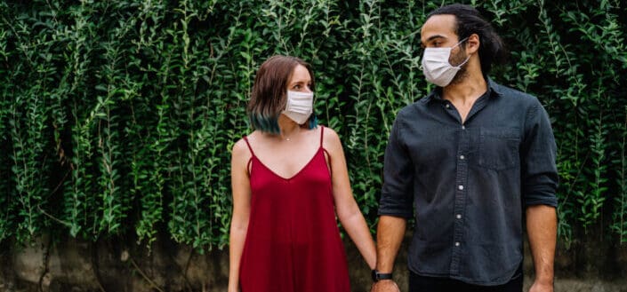 Couple in front of bushes wearing face mask holding hands