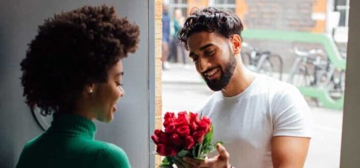 Man on a doorstep giving her girlfriend a bouquet of red roses