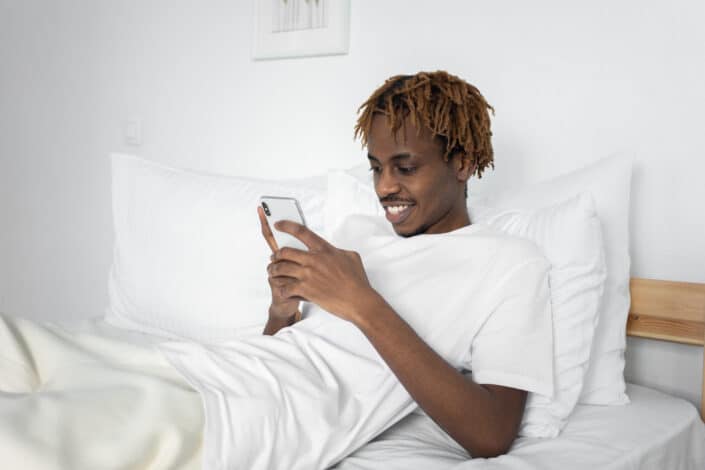 Man in White Using phone while on bed