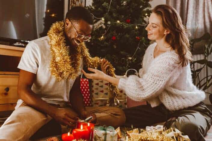 Woman Wrapping a Man in Gold Garland While Wrapping Christmas Presents