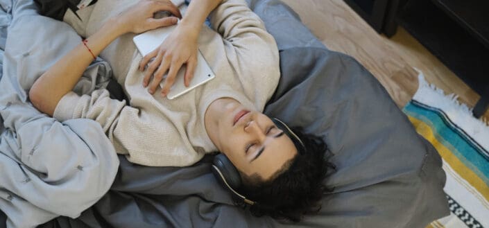 Curly haired guy lying on bed while listening to music with his headphones