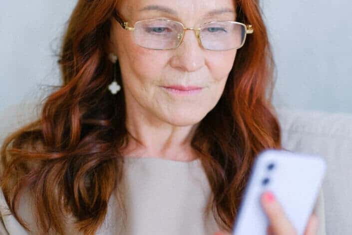 Elderly woman in eyeglasses texting on smartphone