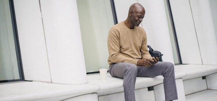 Smiling businessman using phone on street bench