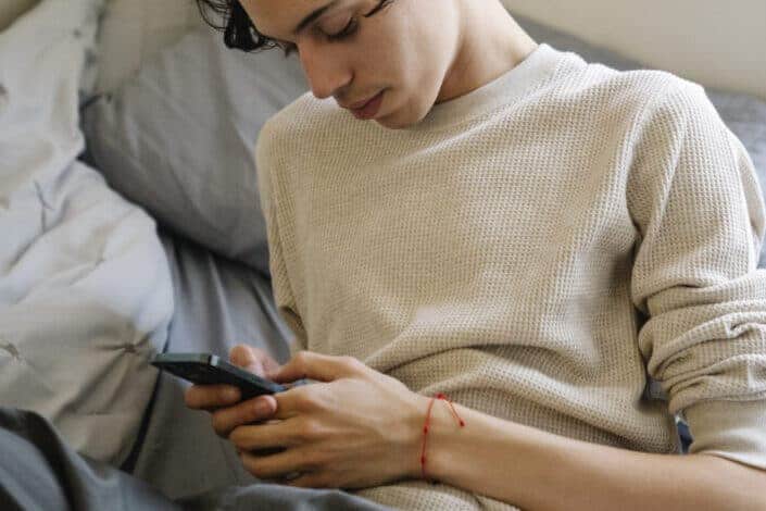 Young Hispanic man using smartphone on bed