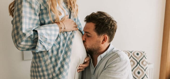 A father kissing her pregnant wife's belly