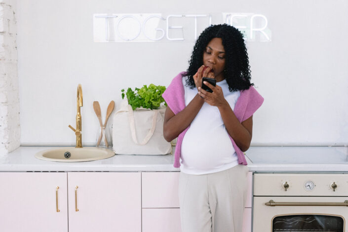Pregnant woman eating an apple while looking at her phone