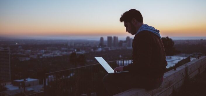 man sitting on concrete brick with open laptop