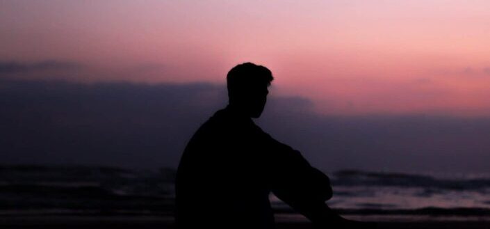 Man Hugging His Knees While Looking Out at the Sea