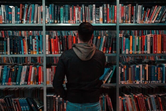 person-wearing-black-and-gray-jacket-in-front-of-bookshelf-stockpack-unsplash