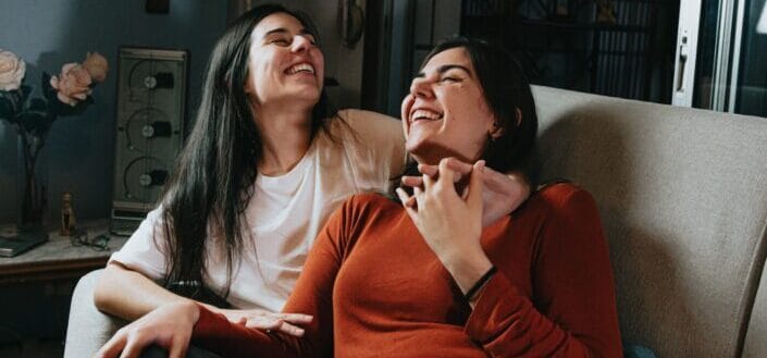 Friends Giggling While Sitting on a Sofa