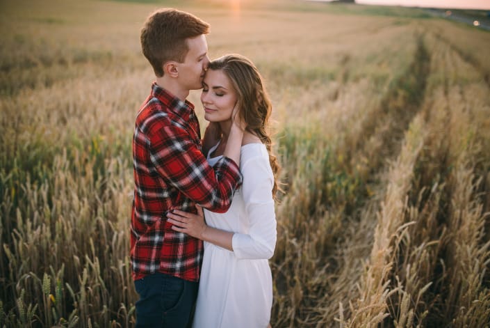 Standing in a wheat field, a man kisses his girlfriend.