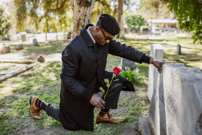 A grieving man kneeling on a grave with red flower