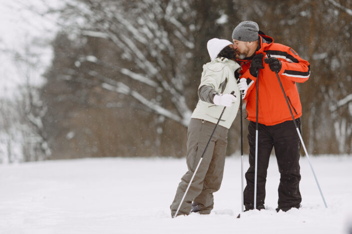 A kissing couple standing on snow covered ground with skis