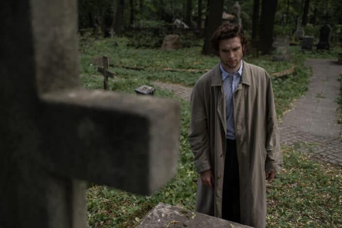 A man in a trench coat looking at a grave