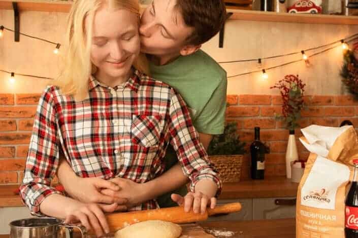 A man kissing his partner while kneading a dough