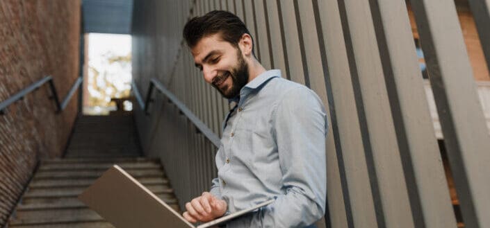 a-smiling-man-using-his-laptop-while-leaning-on-a-handrail-stockpack-pexels