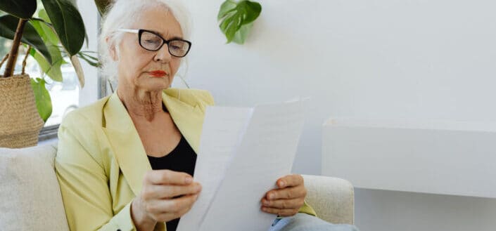 An elderly woman in yellow blazer holding documents