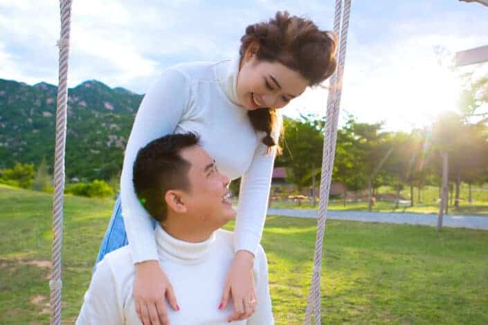cheerful-asian-couple-laughing-on-swing-near-green-meadow-stockpack-pexels