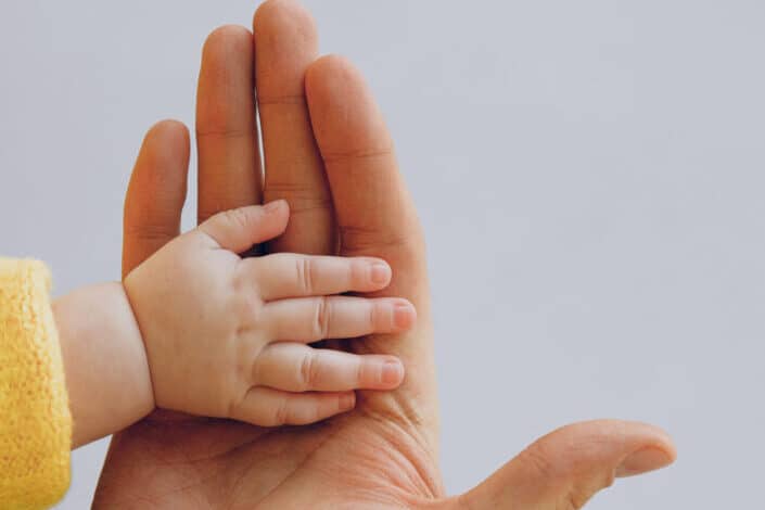 Crop person touch palms with newborn baby on gray backdrop