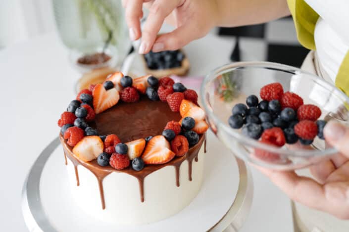 Female confectioner decorating homemade cake with berries